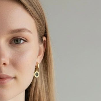 Woman wearing gold earrings and a necklace against a plain background